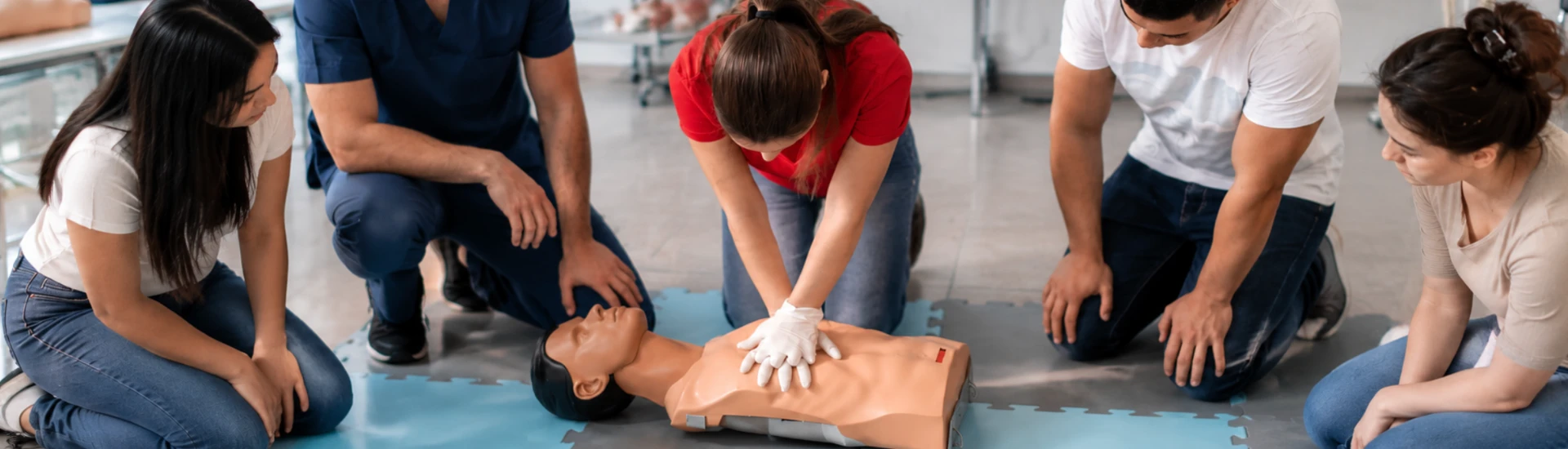A group practising CPR with a mannequin in a bright training classroom